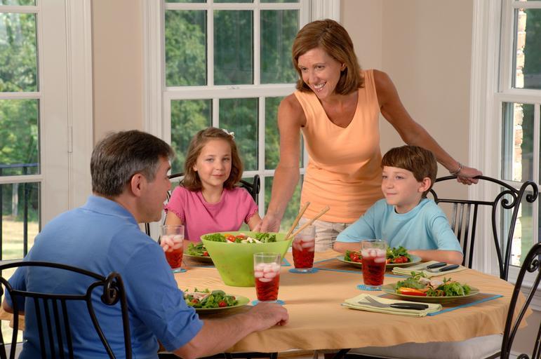 rodina u stolu, rodiče a dvě děti v kuchyni sedí a chystají se jíst, žena donesla salát